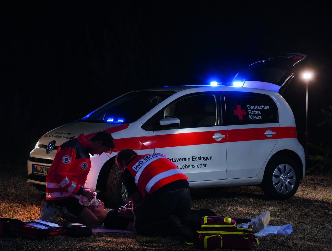 Helfer-vor-Ort des DRK Essingen versorgen nachts einen Patienten neben einem Einsatzfahrzeug.