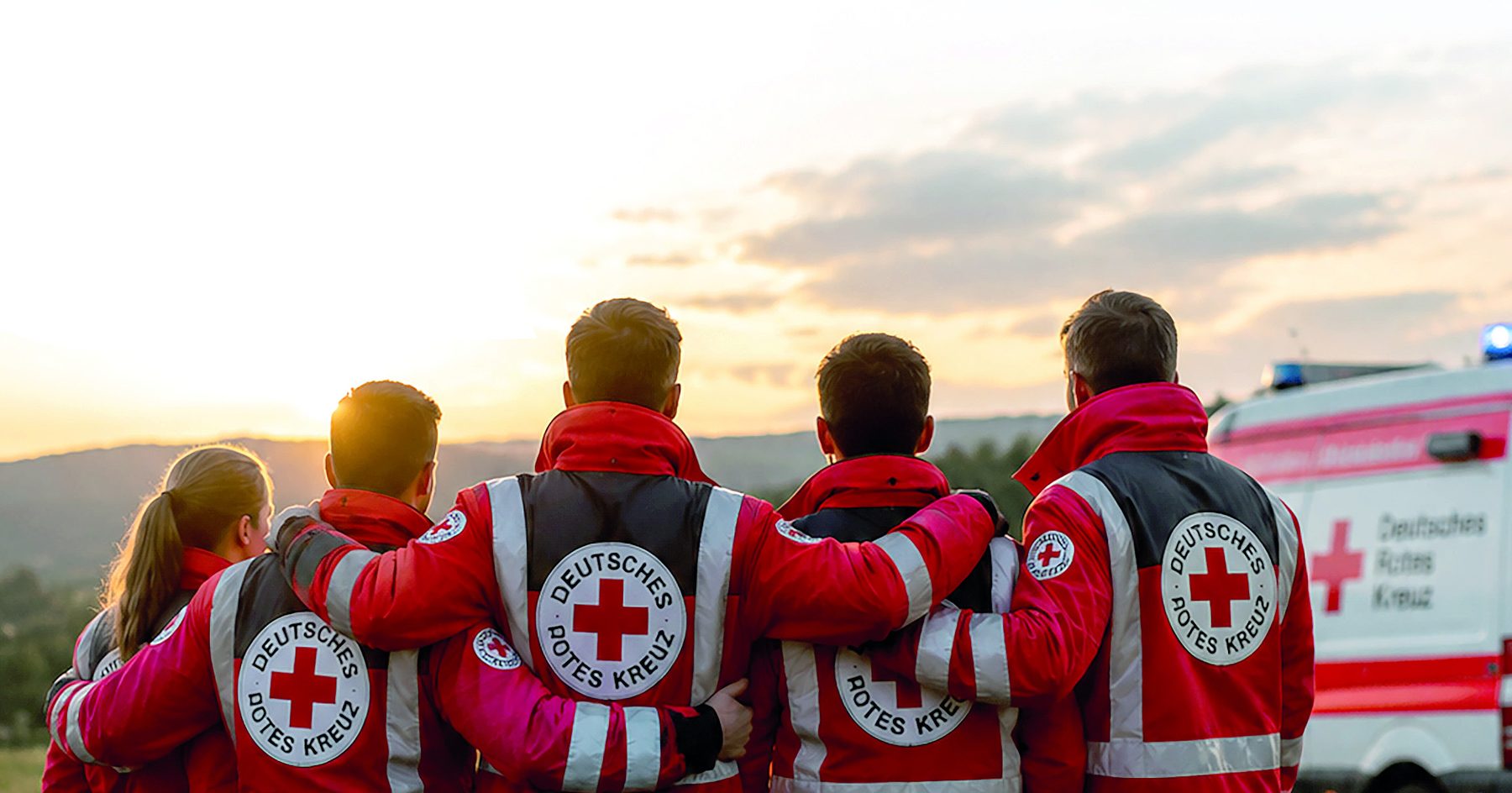 Ehrenamtliche des DRK Essingen stehen gemeinsam vor einem Einsatzfahrzeug bei Sonnenuntergang.